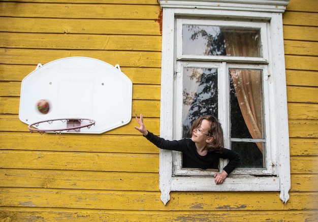 Photo un enfant jouant avec la balle par la fenêtre.