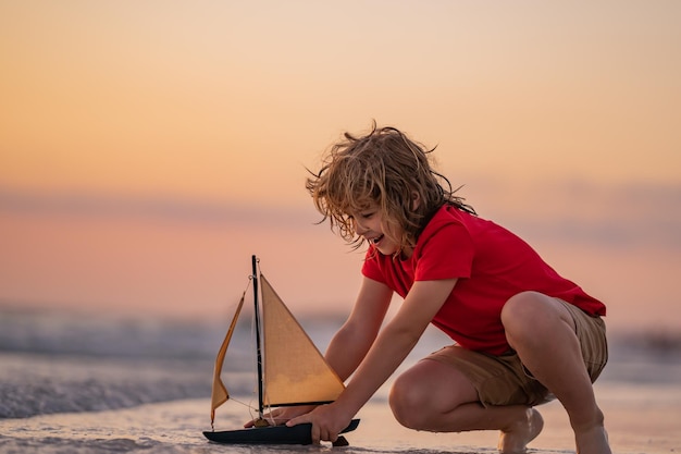 Enfant jouant avec un bateau jouet petit garçon naviguant sur un navire jouet sur l'eau de mer vacances d'été avec les enfants