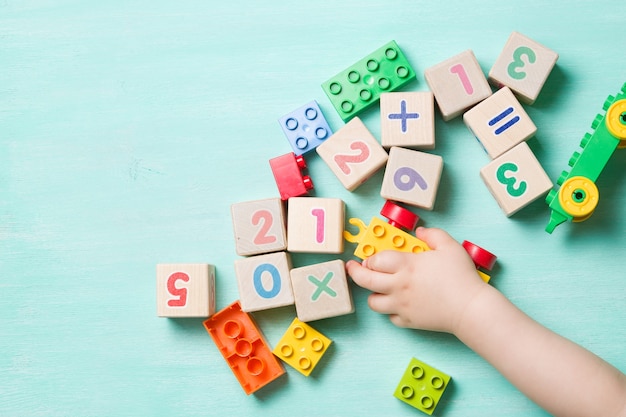 Enfant jouant avec des cubes en bois avec des chiffres et des briques colorées sur un fond en bois turquoise