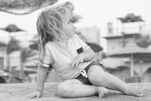 Enfant jouant sur le sable Petit garçon assis sur une plage tropicale Activité d'été sur la plage Vacances loisirs et concept de détente Enfant aux cheveux blonds s'amuser en plein air