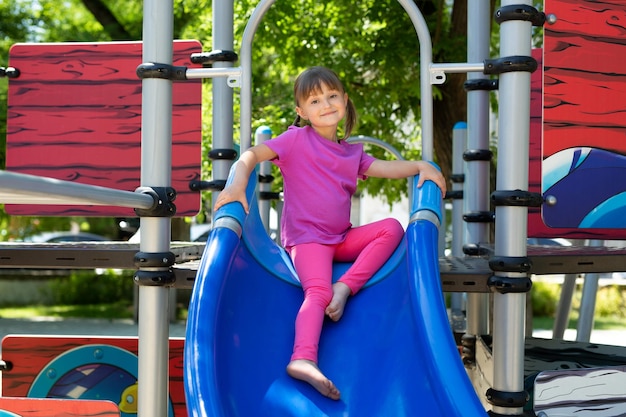 Un enfant joue sur une aire de jeux extérieure Une fille joyeuse et active descend un toboggan