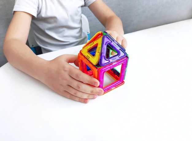 un enfant joue avec un constructeur magnétique sur une table blanche Jeu avec un constructeur magnétique