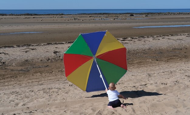 L'enfant joue sur la plage de la mer blanche sous un parapluie