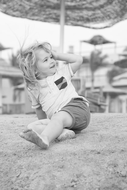 Enfant jouer pieds nus sur la plage de sable aux beaux jours Garçon aux cheveux blonds s'amuser sur le sable Vacances d'été loisirs Activité énergie loisirs Concept d'enfance heureuse