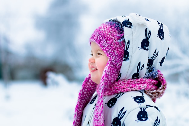 Enfant en jour de neige. Petite fille en blanc neige et rose hatin le parc d'hiver de neige.