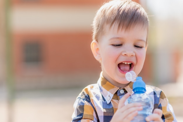 Enfant joyeux boit de l'eau claire d'une bouteille sur une journée ensoleillée dans la nature