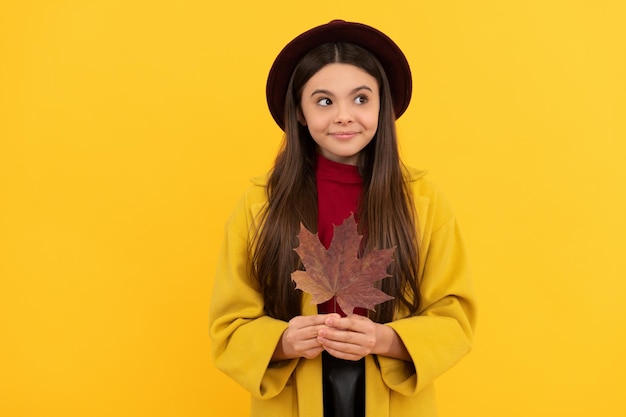 Enfant joyeux en chapeau et manteau avec feuille d'érable d'automne sur fond jaune saison