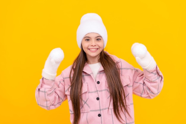 Enfant joyeux en chapeau et mitaines jouant des boules de neige sur fond jaune activité hivernale