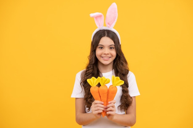 Un enfant joyeux dans des oreilles de lapin tient une carotte sur fond jaune pâques