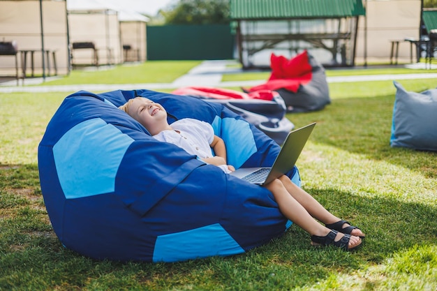 Un enfant joyeux joue sur des poufs colorés dans la rue Un petit garçon regarde des dessins animés sur un ordinateur portable assis sur une chaise dans le parc