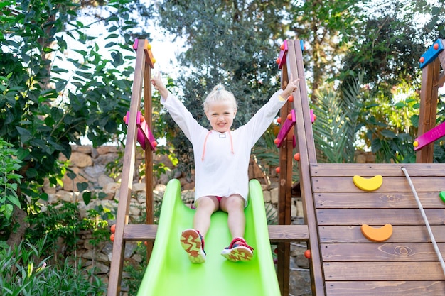 Un enfant joyeux et joyeux joue et roule sur un toboggan sur une plate-forme en bois en été