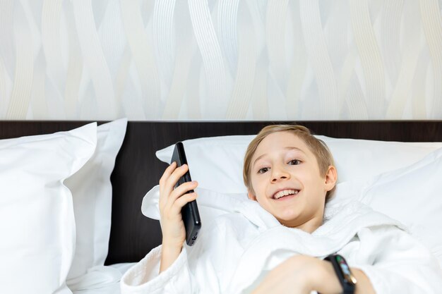 Enfant joyeux parlant au téléphone en position allongée sur le lit dans la chambre d'hôtel