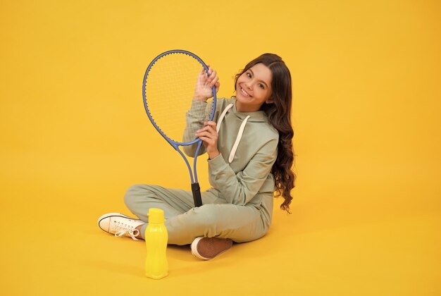 Un enfant joyeux s'assoit dans des vêtements de sport avec une raquette de badminton et une bouteille d'eau sport actif