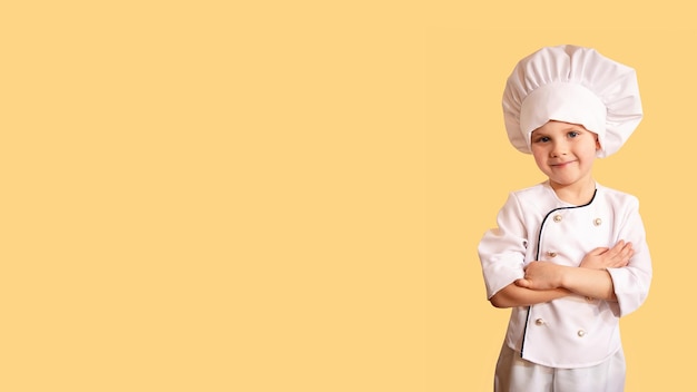 Enfant joyeux souriant en uniforme de chef blanc sur fond jauneGrande bannière