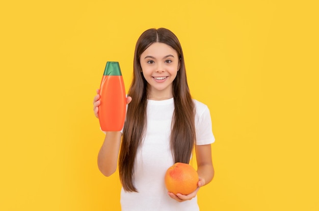 Un enfant joyeux tient une bouteille de revitalisant pour les cheveux et du pamplemousse sur fond jaune vitamine