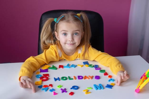 l'enfant a des lettres anglaises étalées sur la table le mot remise des diplômes de vacances est écrit