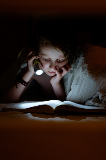 Enfant lisant sous une couverture.