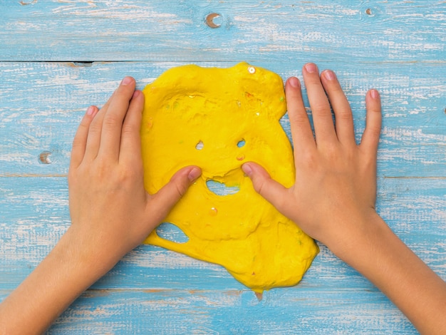 Enfant lisse les mains de slime jaune sur un tableau bleu