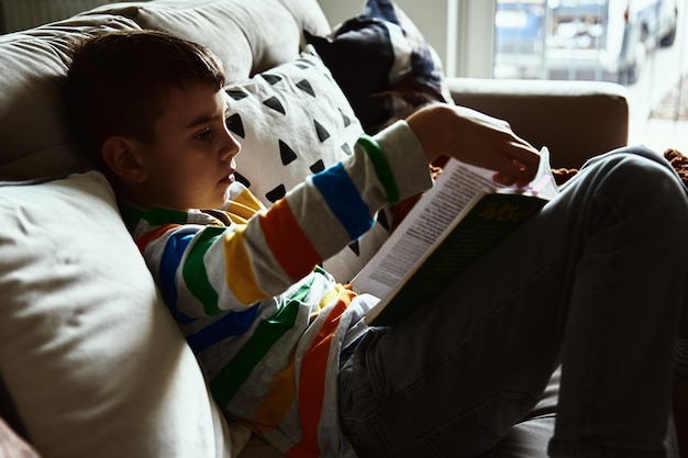 Photo un enfant lit un livre sur le canapé à la maison.