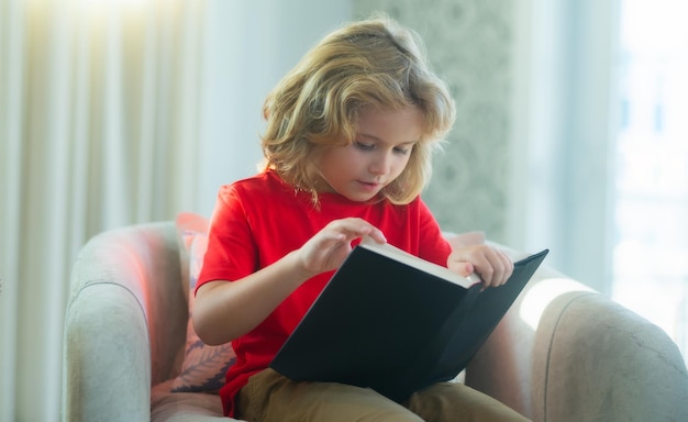 Enfant luant un livre à la maison petit garçon assis sur le canapé dans le salon lisant un livre d'histoires enfant faisant h