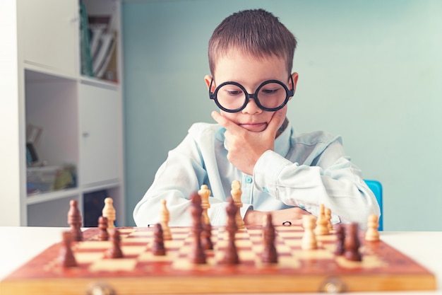 un enfant avec des lunettes joue aux échecs et pense