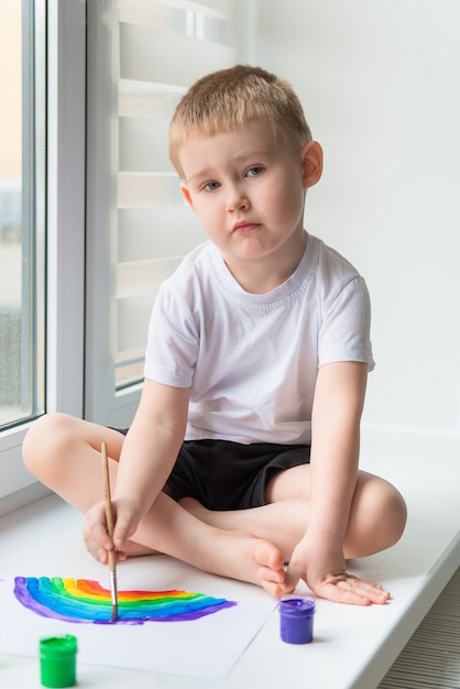 Enfant à la maison dessine un arc-en-ciel sur la feuille de papier