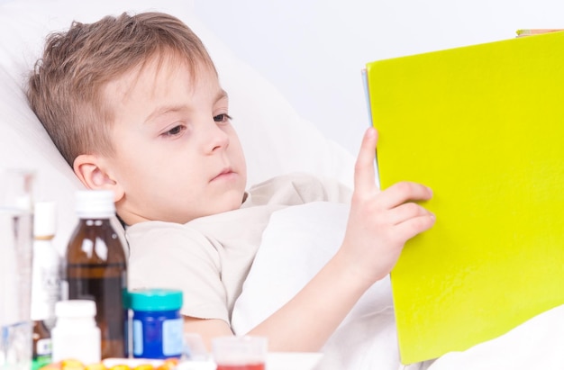 Photo enfant malade couché au lit avec de la fièvre se reposant à la maison enfant souffrant de maladie lisant un livre