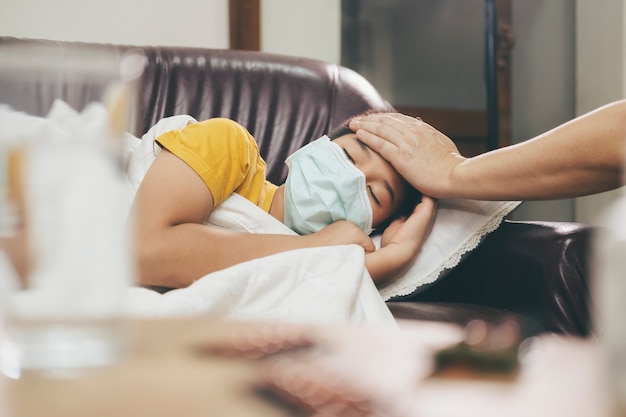 Enfant malade couché dans le canapé-lit avec un masque de protection sur le visage contre l'infection