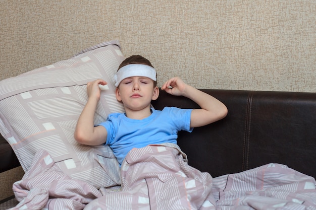 Un enfant malade est allongé sur un lit avec une serviette humide sur le front.