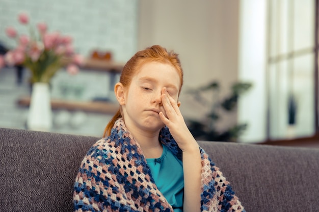 Enfant malade. Fille pâle sans gaieté se frottant le visage tout en se sentant malade