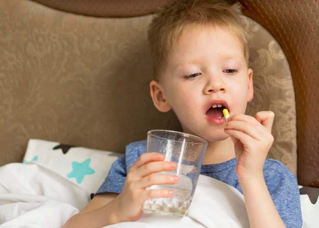 Un enfant malade et triste avec une température et un mal de tête se trouve dans son lit à côté de médicaments et de pilules Virus de la maladie du rhume de la grippe