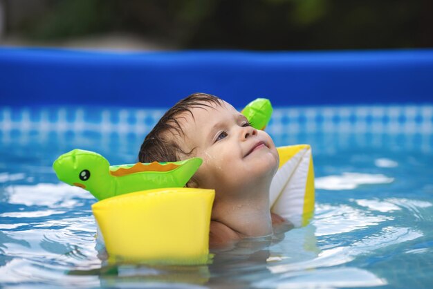 Enfant en manchettes nage dans la piscine dans la cour