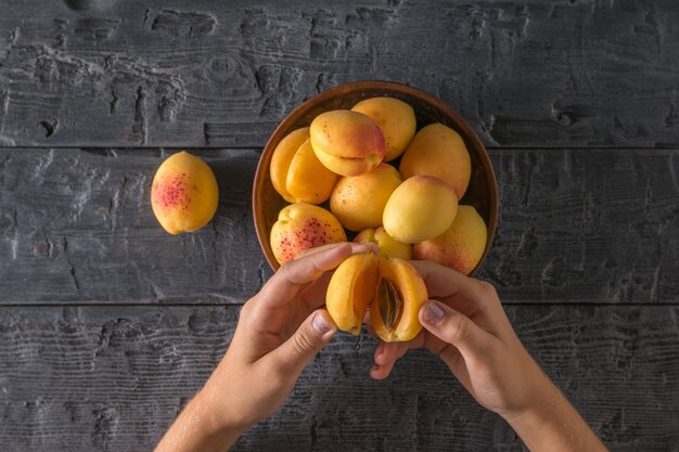 L'enfant mange des abricots mûrs d'une tasse d'argile sur une table en bois