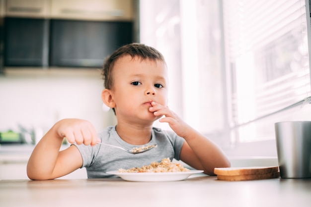 L'enfant mange du pilaf aux carottes dans la cuisine l'après-midi, très savoureux