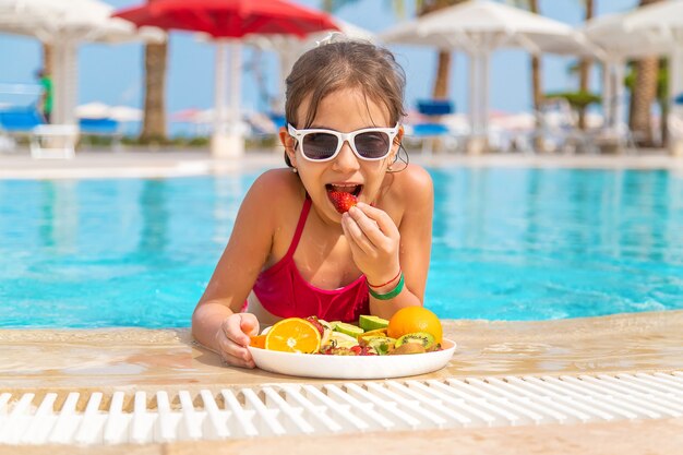 L'enfant mange des fruits près de la piscine