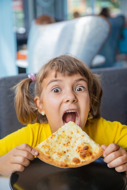 L'enfant mange une pizza au fromage.