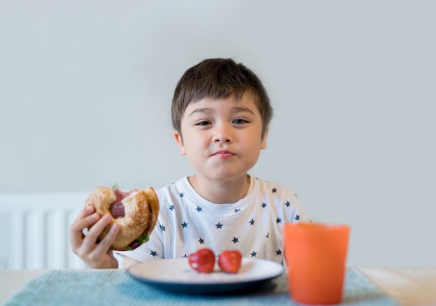 Enfant mangeant des bagels de grains entiers pour son petit-déjeuner, écolier mangeant des beignets en bonne santé Enfant mangeant du pain et du jus de fruits pour son petit-déjeuner. Concept d'enfants sains