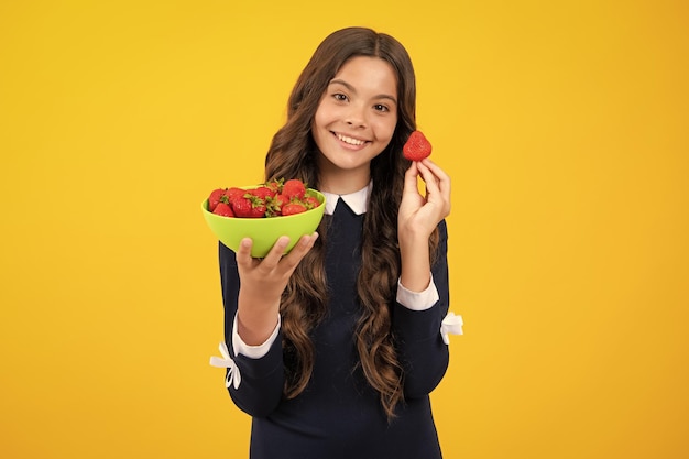 Enfant mangeant des fraises Un enfant adolescent souriant et heureux tient un bol de fraises sur fond jaune Aliments sains et naturels en vitamines biologiques pour les enfants saison des fraises