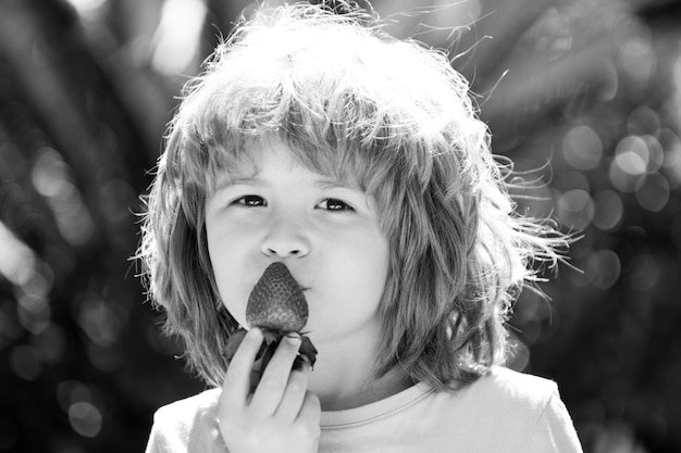 Enfant mangeant des fraises sur fond d'été vert