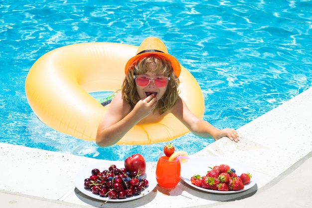 Enfant mangeant des fruits frais sur la piscine d'eau Enfant dans la piscine jouant dans l'eau d'été Vacances et voyageant avec des enfants