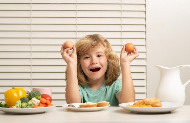 Enfant mangeant des œufs enfant dans la cuisine à la table mangeant des légumes et des fruits pendant le dîner déjeuner