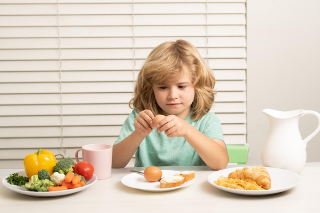 Enfant mangeant des oeufs petit garçon blond drôle prenant son petit-déjeuner lait légumes et fruits aliments sains nu