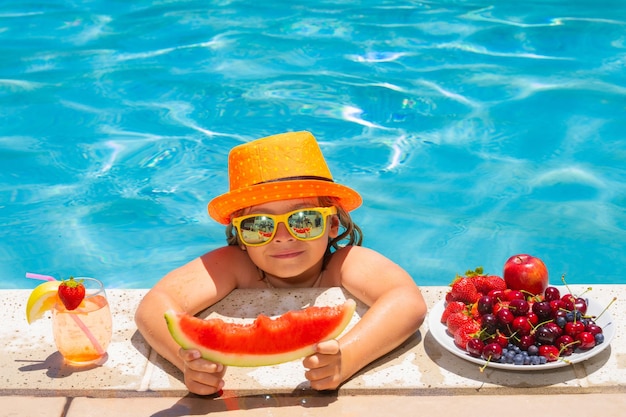 Enfant mangeant de la pastèque Enfant d'été au bord de la piscine mangeant des fruits et buvant un cocktail de limonade Concept de vacances pour enfants d'été Petit garçon se relaxant dans une piscine s'amusant pendant les vacances d'été
