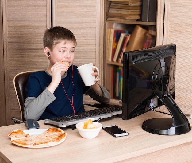 Enfant mangeant de la pizza et surfant sur Internet jouant à des jeux vidéo sur PS Boy dans des écouteurs mangeant de la restauration rapide