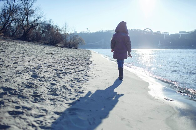 Enfant marchant le long de la rive de la rivière et profitant d'une journée ensoleillée d'hiver