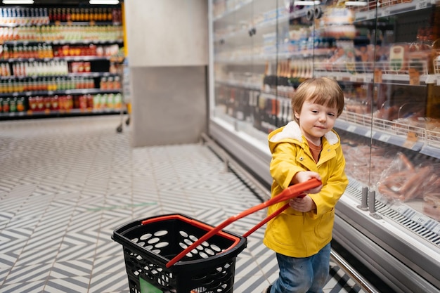 Enfant sur le marché avec un chariot d'épicerie portant une veste jaune et un jean