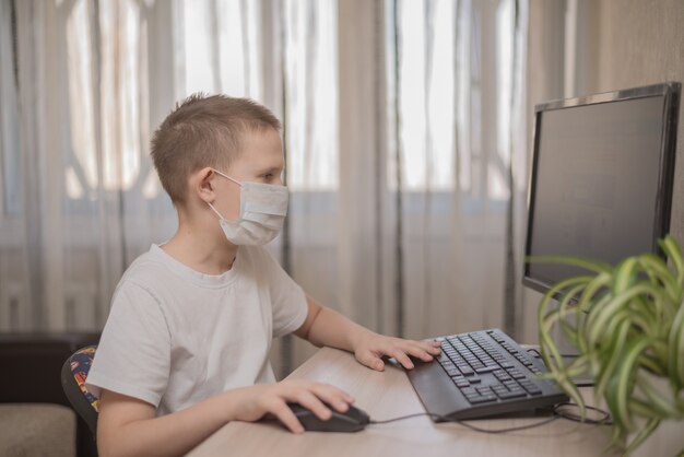 Enfant masqué qui étudie à la maison à table étudie l'école en ligne sur internet