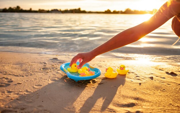 Enfant méconnaissable jouant avec des canards en caoutchouc au bord de la mer.