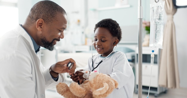 Photo enfant médecin africain et stéthoscope pour ours en peluche sourire ou jouer pour se rétablir de la chirurgie jeu ou respirer enfant patient médecin et garçon avec des jouets parler ou consulter pour la réadaptation dans la clinique