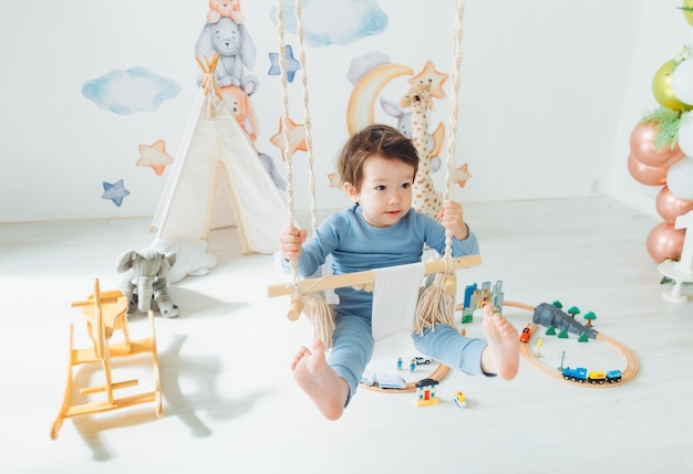 Un enfant mignon asiatique monte dans une balançoire suspendue dans sa chambreBalançoire suspendue pour enfants Un petit garçon se balance dans un hamac à l'intérieur de la chambre des enfants